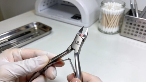 Professional DL cuticle nippers held by a technician against a sanitized salon backdrop