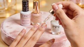 Close-up of a hand applying cuticle oil with nail care products in the background, showcasing beauty and hydration