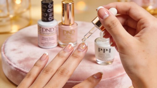 Close-up of a hand applying cuticle oil with nail care products in the background, showcasing beauty and hydration
